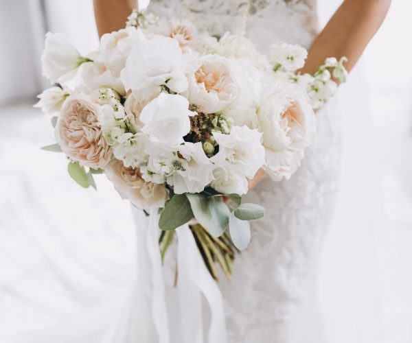 young girl in a white wedding dress holds in her hands a bouquet of flowers and greenery with a ribbon
